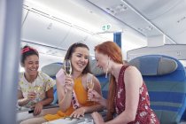 Junge Freundinnen lachen, trinken Champagner in der ersten Klasse im Flugzeug — Stockfoto