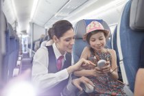 Assistente de bordo ajudando menina passageira com controle remoto no avião — Fotografia de Stock