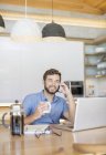 Усміхнений чоловік п'є каву і розмовляє на мобільний телефон у ноутбуці — стокове фото