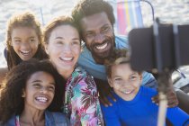 Smiling, happy multi-ethnic family taking selfie with selfie stick camera phone on beach — Stock Photo
