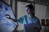 Enfermeira grave usando monitor de tela sensível ao toque, visualização de slides de microscópio — Fotografia de Stock