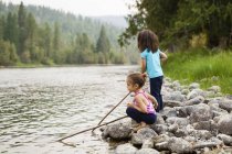 Girl sisters playing with sticks at lakeside — Stock Photo