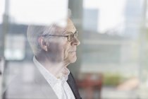 Pensive senior businessman looking out office window — Stock Photo