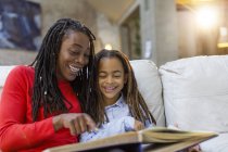 Smiling mother and daughter looking at photo album on sofa — Stock Photo