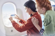 Young women friends using camera phone at airplane window — Stock Photo