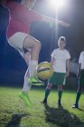 Young female soccer player practicing, jumping and kicking the ball on field at night — Stock Photo