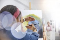 Künstlerin gestikuliert und rahmt Malerei auf Staffelei im Atelier des Kunstkurses — Stockfoto