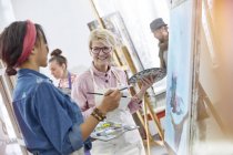 Улыбающиеся художницы с кистями и палитрами живописи в студии художественного класса — стоковое фото