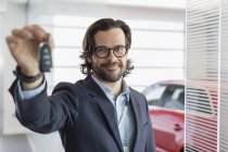 Portrait confident car salesman holding, showing car key in car dealership showroom — Stock Photo