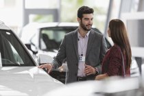 Car salesman showing new car to female customer in car dealership showroom — Stock Photo