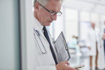 Врач-мужчина с блокнотом смс со смартфоном в больнице — стоковое фото