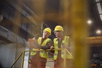 Trabajadores siderúrgicos con portapapeles hablando en plataforma en acería - foto de stock