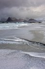 Montañas rugosas detrás del frío, marea de playa oceánica, Storsandnes, Lofoten, Noruega - foto de stock