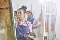 Focused female artist with palette painting at easel in art class studio — Stock Photo