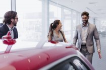 Автомобільний продавець і усміхнені пари клієнтів, дивлячись на новий автомобіль в автосалоні — стокове фото