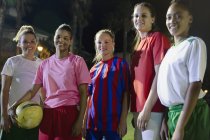 Портрет усміхнений, впевнена молода дівчина футбольних товаришів з м'ячем на полі вночі — стокове фото