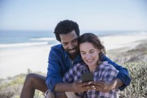 Улыбающаяся многонациональная пара делает селфи с мобильником на летнем пляже — стоковое фото
