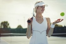 Усміхнена молода тенісистка тримає тенісну ракетку і тенісний м'яч на тенісному корті — стокове фото