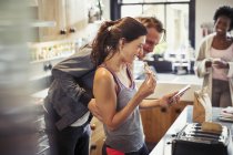 Smiling couple texting with smart phone, eating toast in kitchen — Stock Photo