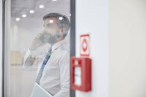 Male supervisor talking on cell phone at window in factory — Stock Photo