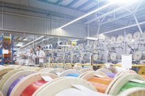 Supervisor masculino e trabalhador verificando inventário atrás de carretéis multicoloridos na fábrica de fibra óptica — Fotografia de Stock
