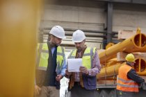 Male foreman and worker reviewing paperwork in factory — Stock Photo