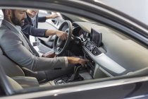 Vente de voiture pointant, expliquant la nouvelle voiture au client masculin dans le siège du conducteur — Photo de stock