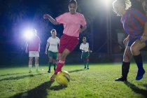 Молодые футболистки, играющие ночью на поле, пинающие мяч — стоковое фото