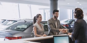Couple arriving, greeting receptionist and handshaking at car dealership showroom — Stock Photo