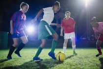 Young female soccer players playing soccer on field at night, kicking the ball — Stock Photo