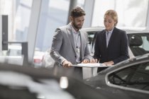 Venditore di auto e cliente femminile revisione dei documenti finanziari contratto in concessionaria auto showroom — Foto stock