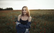 Retrato sorrindo jovem mulher no campo rural com flores silvestres — Fotografia de Stock