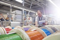 Trabalhador masculino com prancheta verificando carretéis multicoloridos na fábrica de fibra óptica — Fotografia de Stock