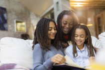 Mother and daughters looking at photo album on sofa — Stock Photo