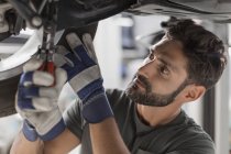 Focused male mechanic fixing wheel underneath car in auto repair shop — Stock Photo