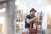 Retrato sorrindo, artista masculino confiante bebendo café em estúdio de arte — Fotografia de Stock