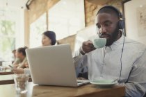 Hombre con auriculares usando portátil y beber café en la cafetería - foto de stock