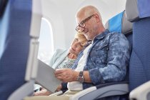 Affectionate mature couple sleeping and reading on airplane — Stock Photo
