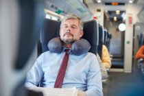 Втомлений бізнесмен з подушкою для шиї спить на пасажирському поїзді — стокове фото