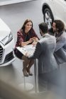 Vendedor de coches dando llaves de coche a cliente femenino sonriente en sala de exposición de concesionarios de coches - foto de stock