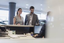 Couple at reception desk in car dealership showroom — Stock Photo