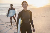 Retrato mujer segura en traje de neopreno con tabla de surf en la soleada playa de verano con la familia - foto de stock