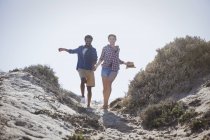 Грайлива, енергійна багатоетнічна пара бігає і тримає руки на сонячній літній пляжній стежці — стокове фото