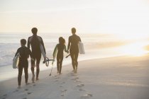 Familia en trajes de neopreno caminando con tablas de surf en la soleada playa del atardecer de verano - foto de stock