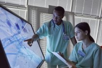 Krankenschwestern mit Klemmbrett begutachten vergrößerte Objektträger auf Computermonitor — Stockfoto