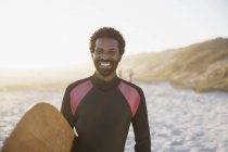 Ritratto sorridente, surfista sicuro di sé con tavola da surf sulla soleggiata spiaggia estiva — Foto stock