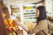 Улыбающаяся молодая женщина покупает яблоки в продуктовом магазине — стоковое фото