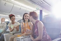 Молоді жінки друзі п'ють шампанське в першому класі на літаку — стокове фото