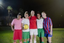Retrato sonriente, confiada joven compañeras de equipo de fútbol con pelota en el campo por la noche - foto de stock