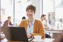 Ritratto donna d'affari sorridente che beve caffè lavorando al computer portatile nel caffè — Foto stock